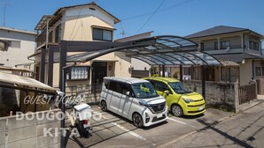 Een woonwijk met een overdekte parkeergarage, een witte bus en een gele auto geparkeerd voor een twee verdiepingen tellend huis.