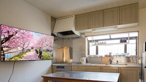 Een keuken met houten kastjes, een inbouwoven, een raam met servies, en een tv waarop een kersenbloesem te zien is.