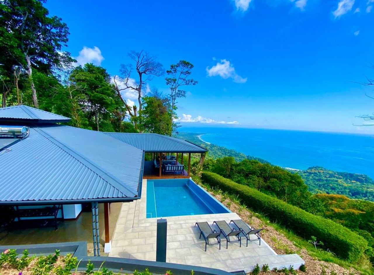 Ein modernes Haus mit Pool, überdachter Terrasse und Meerblick.