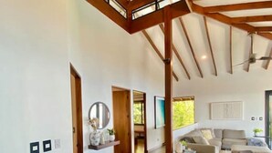 Amplia sala de estar con techo alto y vigas de madera a la vista, un ventanal grande y una zona de estar con sofás y una mesa de centro.
