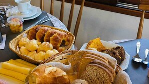 A breakfast table with various breads, pastries, and a cup of coffee. - Pousada Canajurê (Florianópolis)