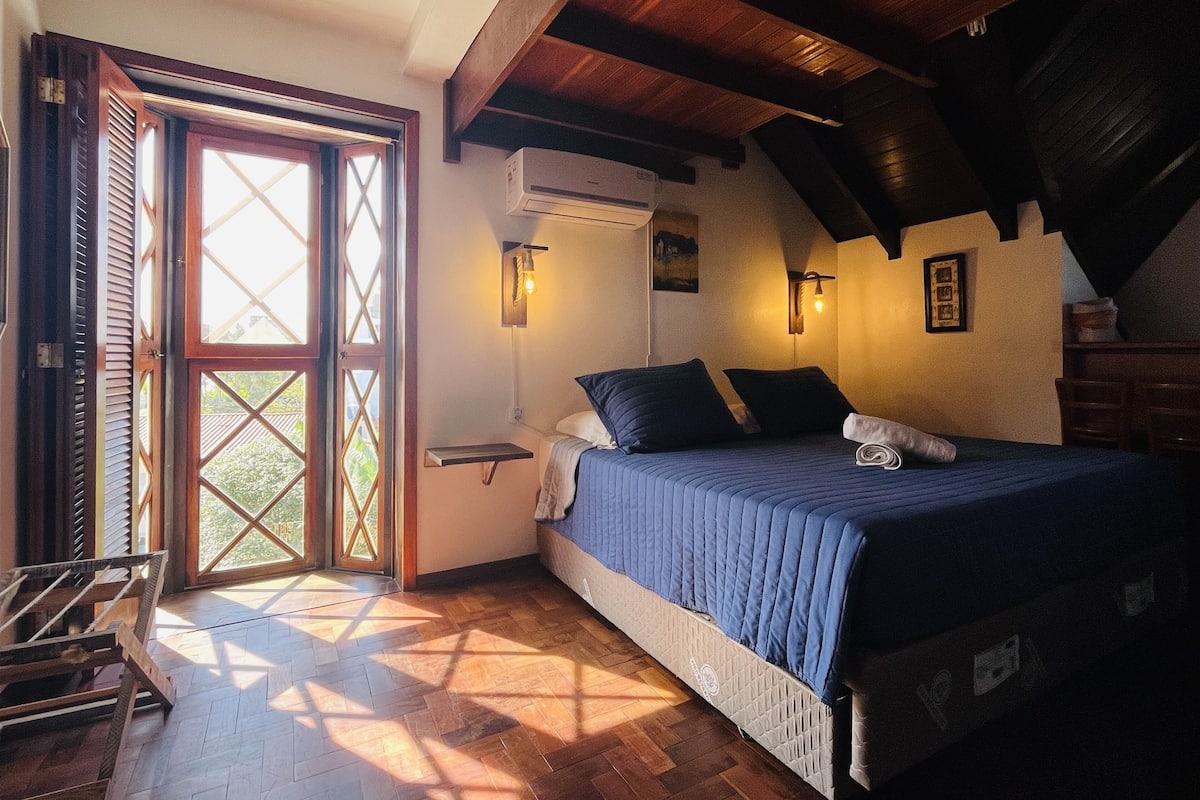 A bedroom with a bed, a wooden ceiling, a window, and a wall-mounted air conditioner.