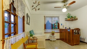 A cozy kitchen with wooden furniture, a ceiling fan, and decorative elements like lace curtains and wall art. - Pousada Canajurê (Florianópolis)
