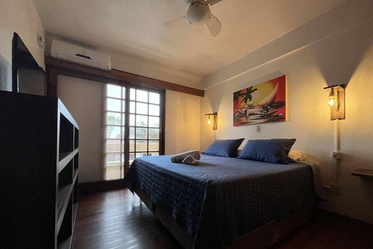 A bedroom with a bed, a TV, a painting, and a window.