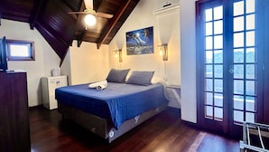 A bedroom with a bed, a ceiling fan, a painting, a window, and a door. - Pousada Canajurê (Florianópolis)
