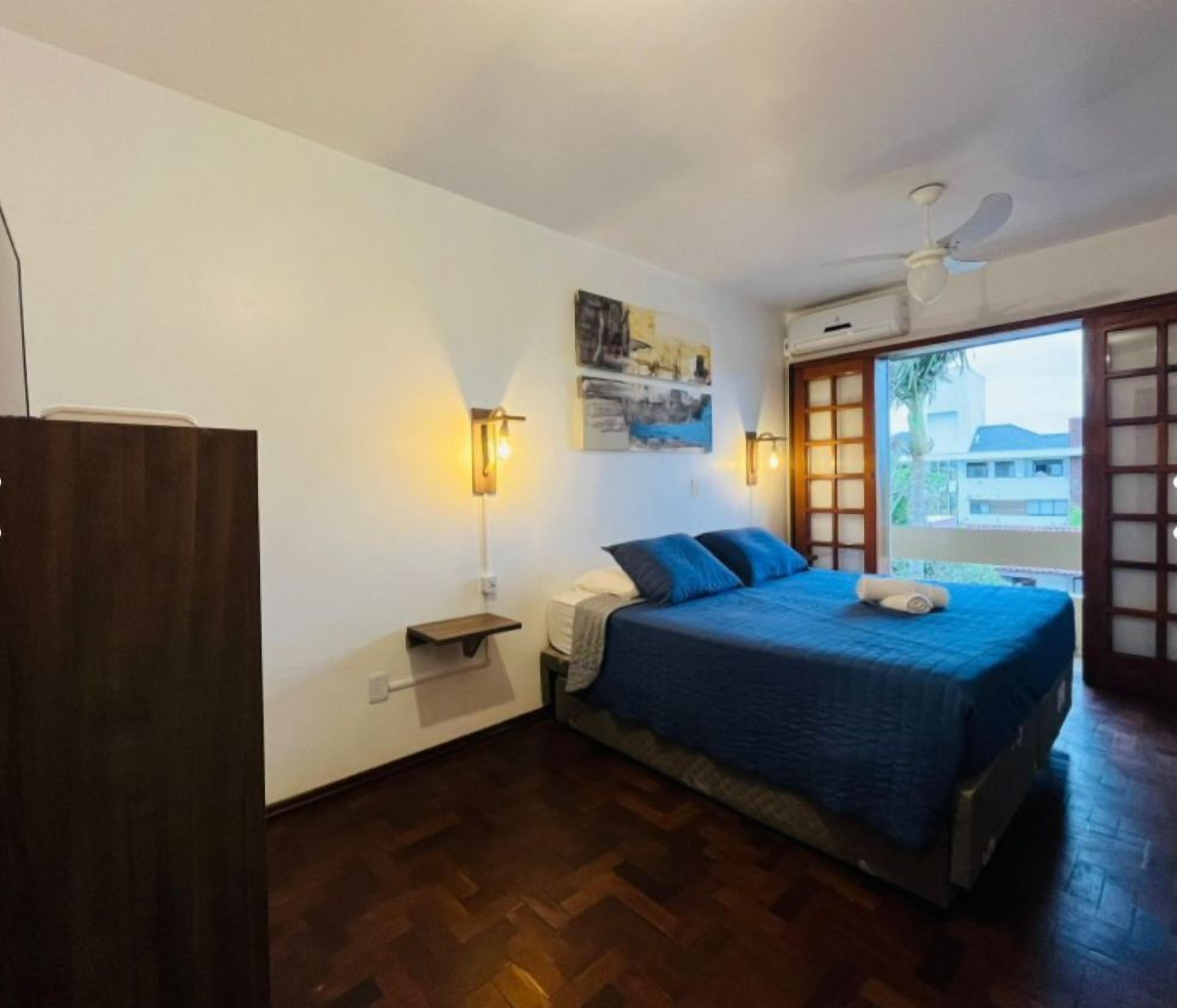 Une chambre à coucher comprenant un lit, une table de chevet, une lampe fixée au mur et une fenêtre donnant sur un paysage agréable.