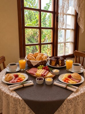 A breakfast table set with various food items, a window with lace curtains, and a view of greenery outside. - Pousada Canajurê (Florianópolis)