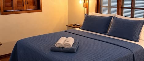 A bedroom with a bed, a ceiling fan, an air conditioning unit, a nightstand, and a window with blinds.