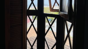A view through a window with a geometric pattern, revealing a brick-paved area and buildings in the distance. - Pousada Canajurê (Florianópolis)