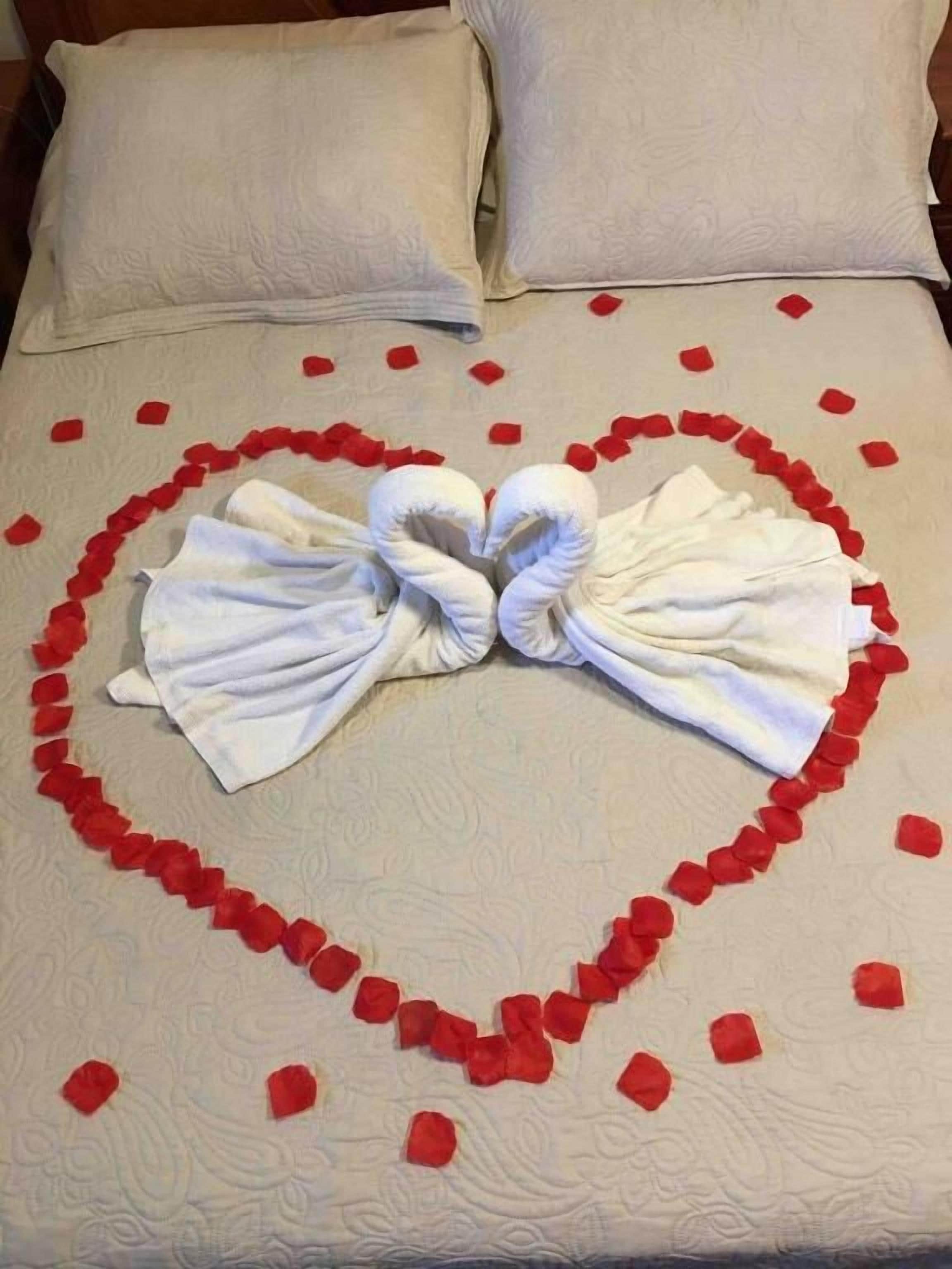 Un letto con una composizione a forma di cuore di petali di rosa e asciugamani.