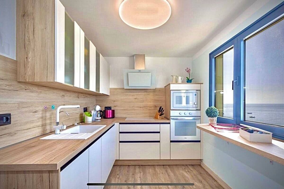 Una cocina moderna con encimera de madera, armarios blancos, horno integrado y ventana con vistas.