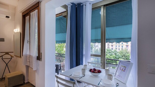 Ein Essbereich mit einem für zwei Personen gedeckten Tisch, einem Fenster mit Vorhängen und Blick auf Gebäude und Bäume.