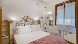 Ein Schlafzimmer mit einem Bett, einem Schrank, einem Spiegel und einem Fenster mit Vorhängen.