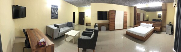 A hotel room with a bed, sofa, armchair, small table, and a TV.