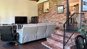 Ein Wohnzimmer mit Backsteinwand, einer Couch, einem Fernseher und einer Treppe.