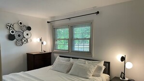 Ein Schlafzimmer mit einem Bett, zwei Nachttischen, einer Kommode, einem Fenster mit Jalousien und Wanddekoration.