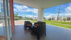 Un espace extérieur aménagé, abrité et doté de deux fauteuils en osier et d’une table, offrant une vue sur un jardin paysager et des bâtiments modernes.