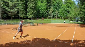 A tennis court with a net, surrounded by trees and a fence.