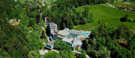 An aerial view of a hotel with a swimming pool, surrounded by lush greenery and hilly terrain.