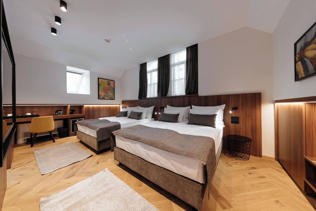 Ein modernes Hotelzimmer mit zwei Betten, einem Schreibtisch und einem Sessel.