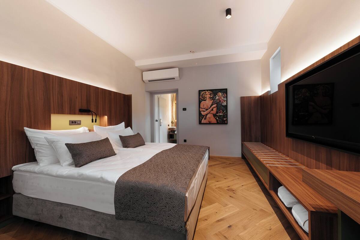 Ein modernes Schlafzimmer mit einem großen Bett, Holzwandverkleidung, einem Flachbildfernseher und einer Bank mit Handtüchern.