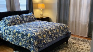 A bedroom with a large bed, a nightstand with a lamp, and a patterned rug. - Peaceful home with an amazing yard near downtown San Antonio. Pet Friendly! (San Antonio)