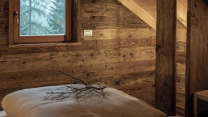 Habitación de cabaña de madera con techo inclinado, una ventana con vista a un bosque y una cama con una rama encima.