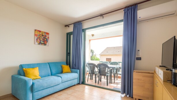 Un salon avec un canapé bleu, un coussin jaune et un tableau accroché au mur.