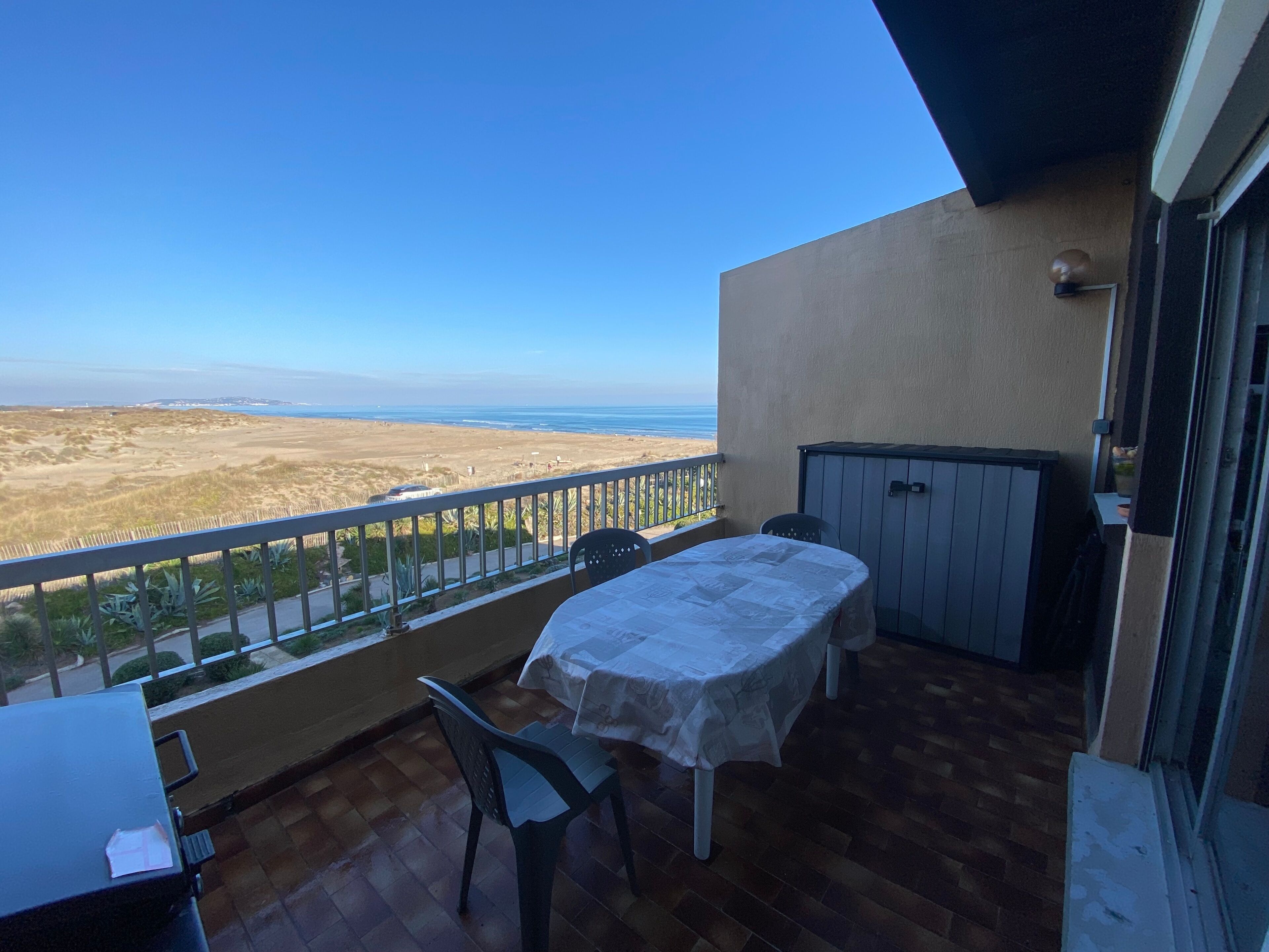 A balcony with a table and chairs, overlooking a beach and ocean.