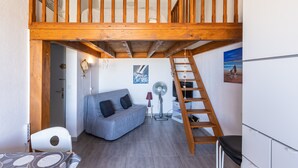 Ein Loft-Zimmer mit einer Holztreppe, einem grauen Sofa, einem kleinen Tisch und einem Ventilator.