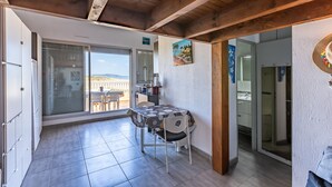 Ein Essbereich mit Tisch und Stühlen, Blick durch eine Glastür auf einen Balkon im Freien und ein Gemälde an der Wand.