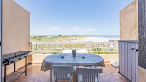 Eine Terrasse im Freien mit Tisch, Stühlen, einem Grill und Blick auf den Strand.