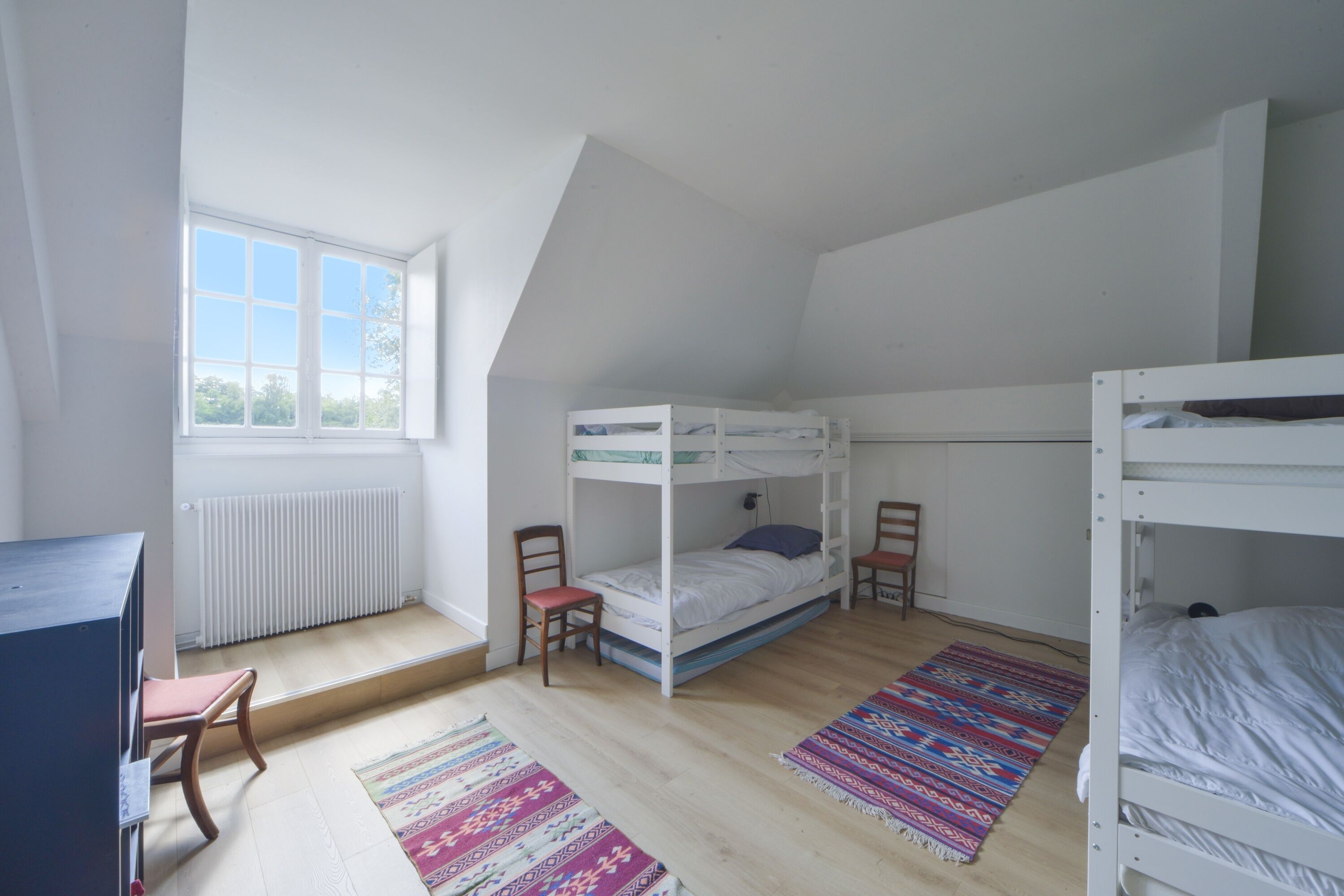 A dormitory room with bunk beds, a desk, and a window.