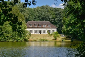 Un grande edificio bianco con tetto simmetrico e numerose finestre, immerso nel verde e affacciato su un corpo d'acqua.
