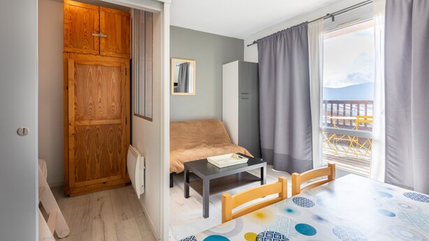 A compact room with a bed, a small table, a chair, a wardrobe, and a balcony with a view. - Zénitude - Appartement au pied des pistes (Les Angles)