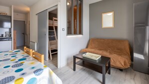 A compact living space with a bed, a sofa, a table, a wardrobe, and a kitchen area. - Zénitude - Appartement au pied des pistes (Les Angles)