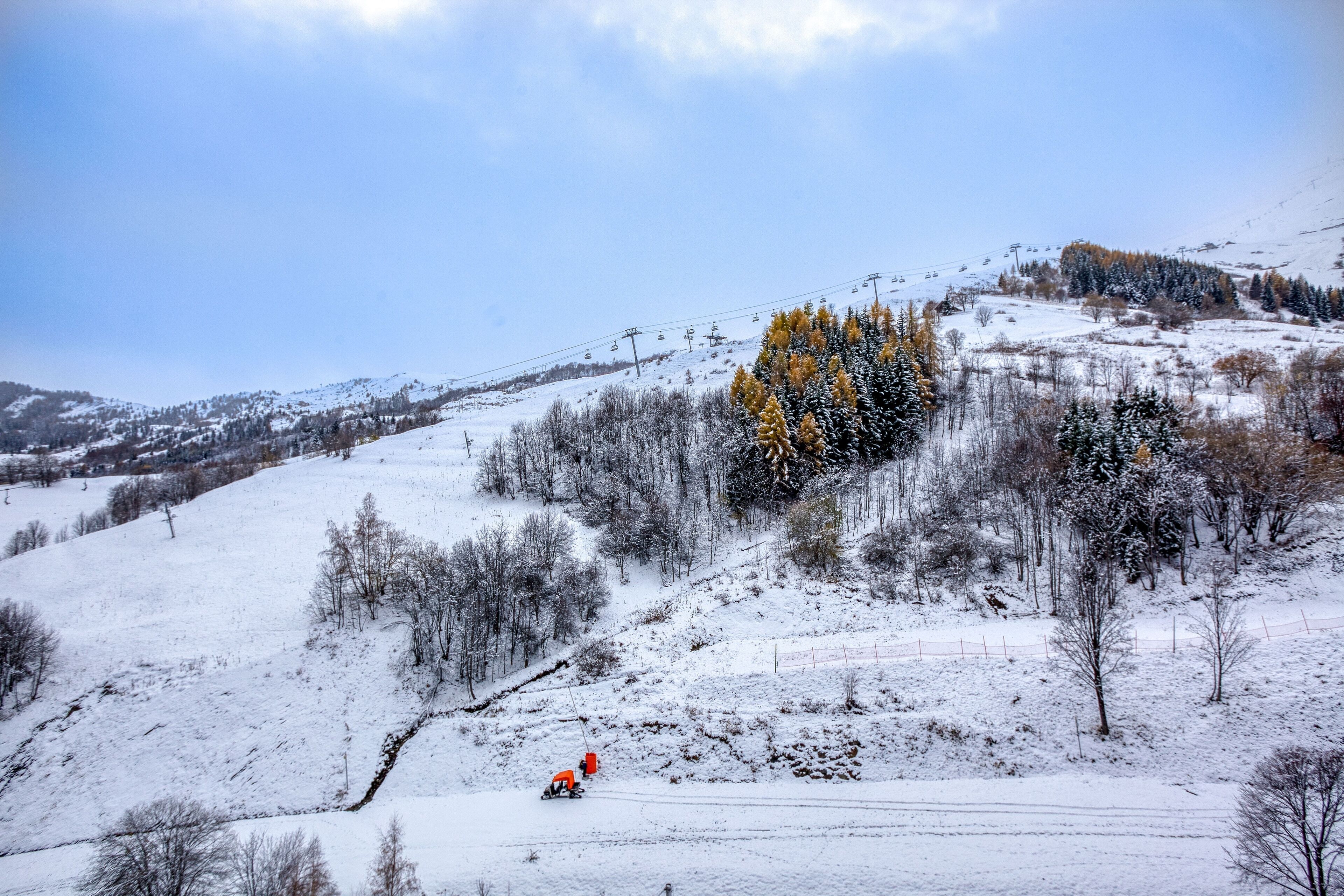 Schneebedeckte Landschaft mit einer Seilbahn, Bäumen und einer Person in orangefarbener Ausrüstung.