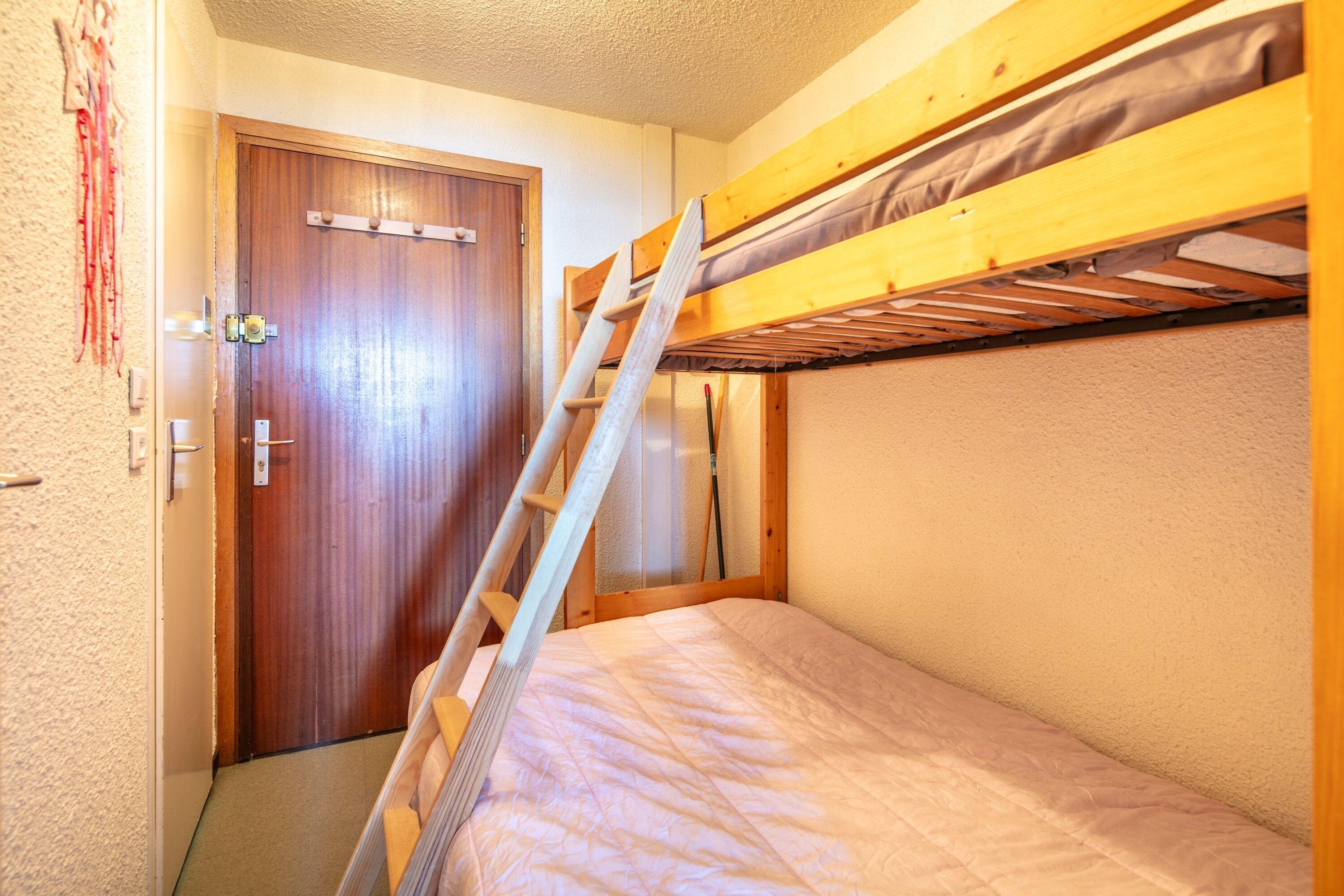 A bunk bed room with a wooden ladder, a door, and a wall-mounted shelf.