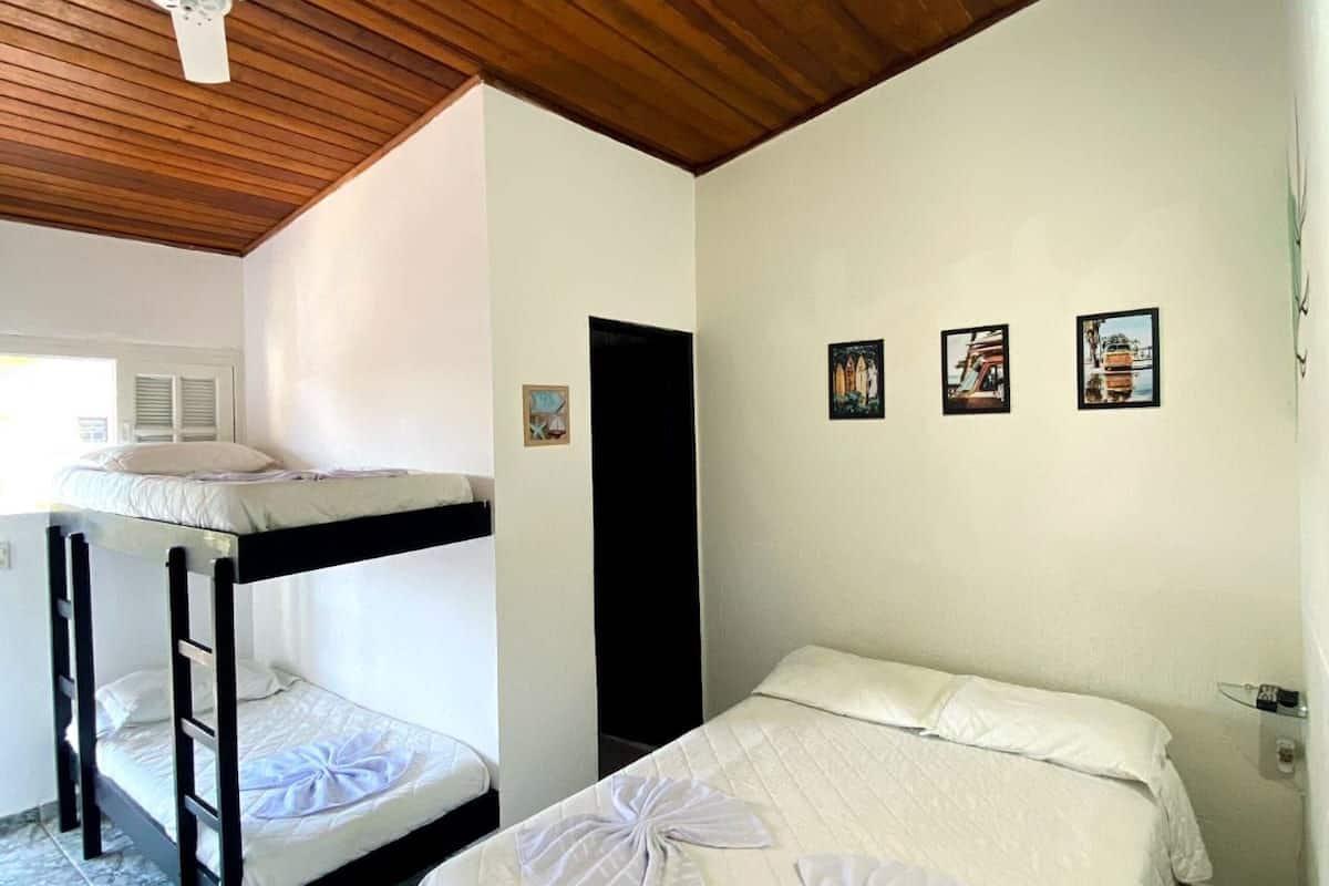 A room with a bunk bed, a single bed, a ceiling fan, and a wooden ceiling.
