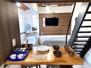 Habitación pequeña con cama, televisor, ventilador y comedor con platos y fuentes.