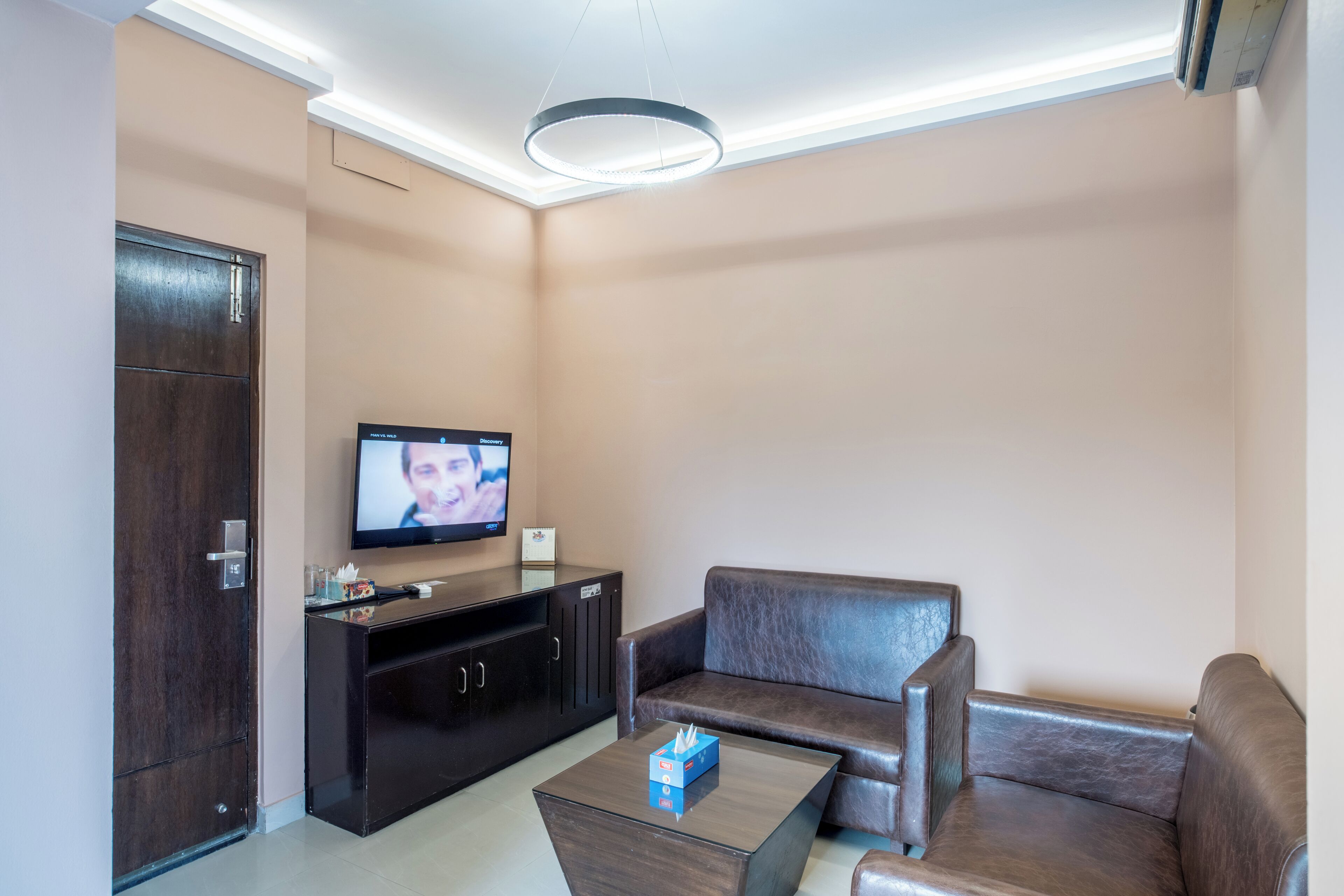 Una sala de estar moderna con un mueble bajo de madera oscura, un sofá de cuero, una mesa de centro y un televisor de pantalla plana montado en la pared.