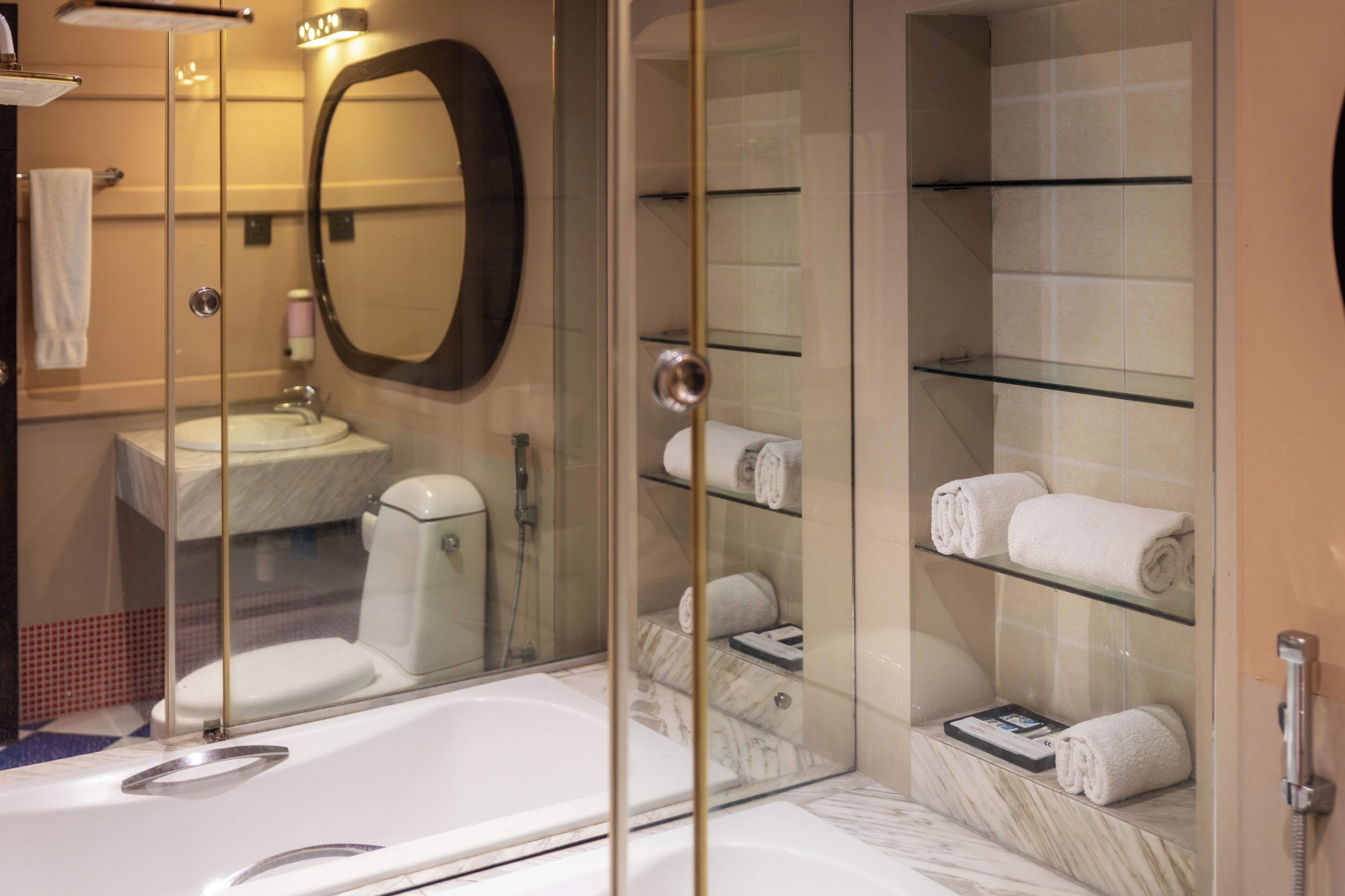 Un baño moderno con ducha envuelta en vidrio, una bañera amplia, inodoro y un estante de vidrio con toallas.