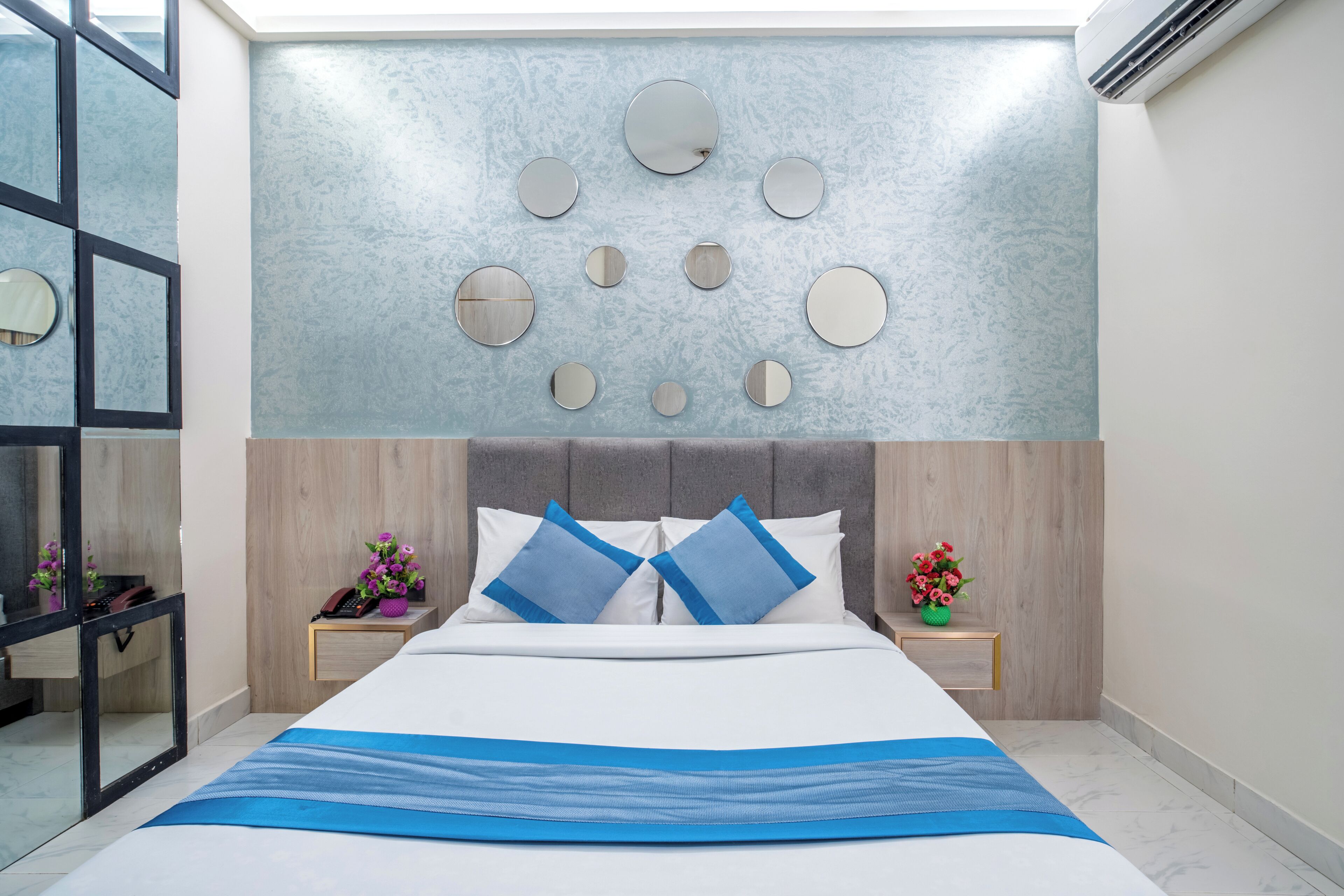 A modern bedroom with a large bed, a wall-mounted mirror, and a decorative wall panel.
