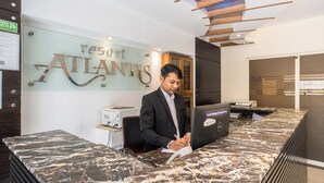 Un comptoir d’accueil avec un plateau en marbre, une enseigne indiquant « complexe hôtelier ATLANTIS », et un homme assis derrière le comptoir.