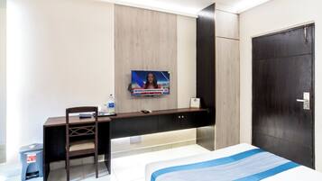 Habitación de hotel con cama, escritorio, silla, televisor montado en la pared y una puerta.