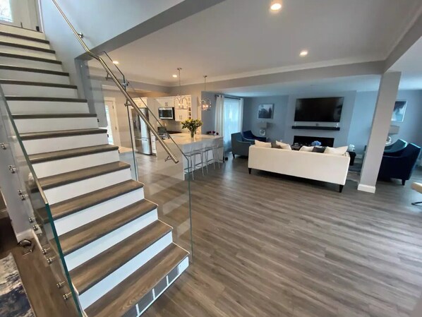 A modern living room with a staircase, a kitchen, and a dining area.