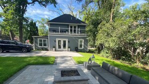 Une maison à deux étages avec un porche à l’avant, une allée et un jardin aménagé comprenant un foyer extérieur.
