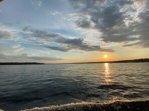 Un coucher de soleil sur une étendue d’eau calme, avec une côte visible au loin.
