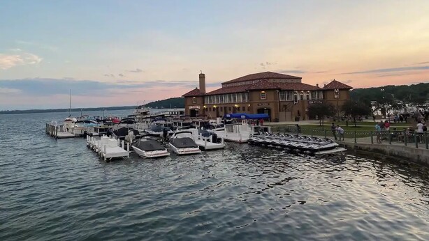 Un port de plaisance avec des bateaux amarrés, un bâtiment doté d’un toit en tuiles et un parc au bord de l’eau.