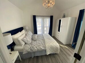 Une chambre à coucher avec un lit, une armoire, un lustre et une fenêtre avec des rideaux.